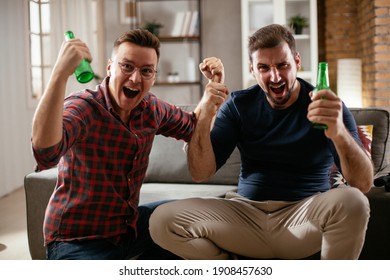 Two Young Friends Enjoying At Home. Men Drinking Beer And Watching Sports Game On Tv.	