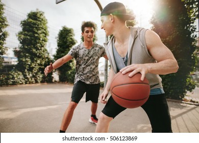 Two young friends playing basketball on court outdoors and having fun. Streetball players having a basketball game.