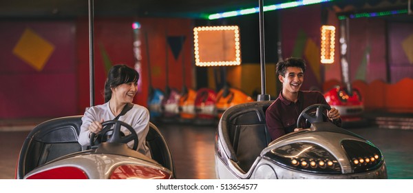 Two young friends riding bumper cars at amusement park. Happy young man and woman driving bumper cars.