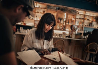 Two Young Friends Sitting Together At The Table In A Bar In The Evening Reading Menus