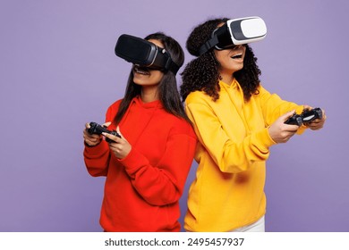 Two young gambling happy little kid teen girls women they wearing red yellow hoodie casual clothes watching in vr headset pc gadget isolated on plain pastel light purple background. Lifestyle concept - Powered by Shutterstock