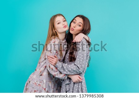 Two young girl friends hugging and kissing isolated over blue turquoise background