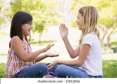 Two young girl friends sitting outdoors playing patty cake smiling - Powered by Shutterstock