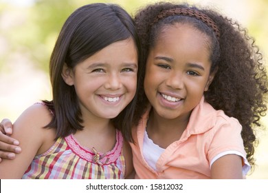 Two young girl friends sitting outdoors smiling