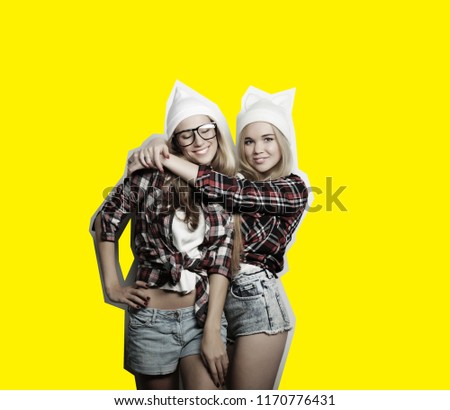 Two young girl friends standing together and having fun. Looking at camera. Yellow background, art collage.