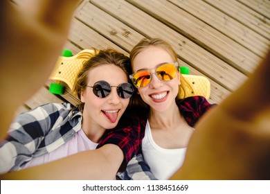 Two young girl in hipster outfit making selfie while lying with on wooden pier - Powered by Shutterstock