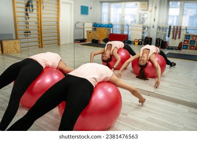 Two young girl laying on swiss balls and stretching their backs 