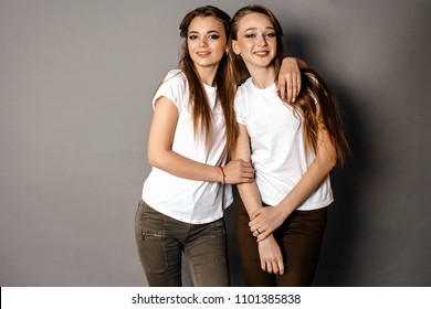 two young girlfriend girls in white t-shirts on a gray background posing, hugging and smiling. suitable for mockup - Shutterstock ID 1101385838