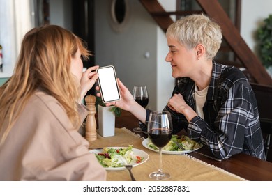 Two Young Girlfriends Lesbians Showing Photos On Smartphone During Romantic Date Dinner Discussing Skin Care Problems And Beauty Tips. Best Friends, LGBT Relationship And Friendship