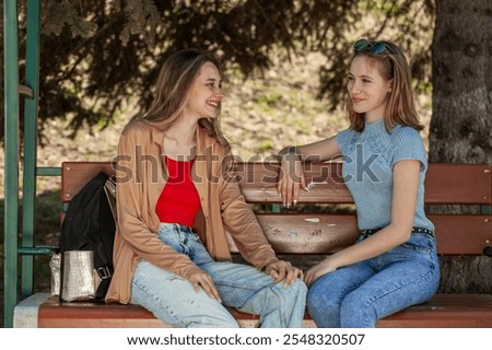 Two young girlfriends are talking while sitting on a bench
