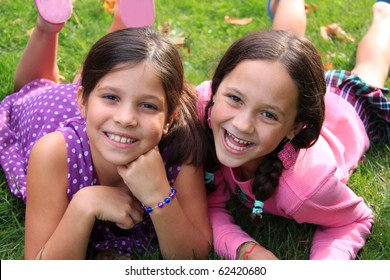 Two young girls in the ages of ten and eight that could be sisters or best friends laying on the grass and smiling whitle wearing colorful clothing