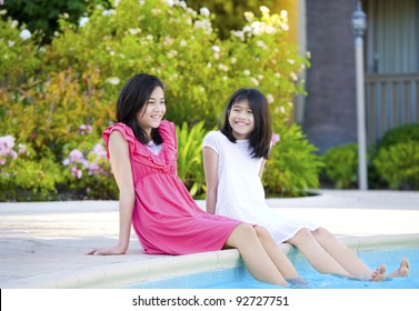 Two young girls, biracial, part- Asian, enjoying time sitting by pool. - Powered by Shutterstock