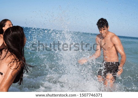 Two young girls and a young boy are splashing and playing with water in the sea