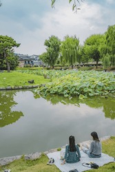 The Two Young Girls Enjoying A Picnic Near The Pond In South Korea