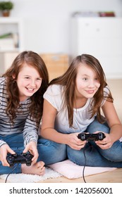 Two Young Girls Happily Playing Video Games In A Console Sitting On The Living-room Floor