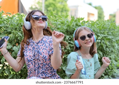 Two young girls, siblings or friends, enjoying a beautiful day in the park together, listening to music on headphones and sharing a hug. - Powered by Shutterstock