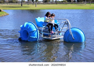 Two young girls sisters (age 11-12 and 7-8) riding on a big wheel aqua bike water tricycle  over a lake waters.