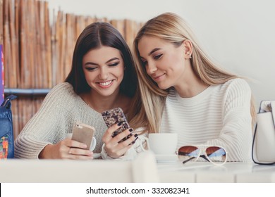 Two young girls using smart phone at the outdoors cafe. Two women after shopping with shopping bags sitting in cafe with coffee and using smartphone