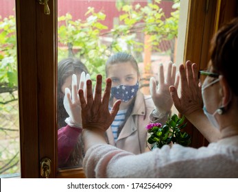 Two Young Girls Visit An Elderly Grandmother, Looking At Her Through The Window In The Hope Of Hugging Her