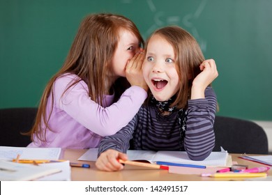 Two young girls whispering and sharing a secret during class in school - Powered by Shutterstock