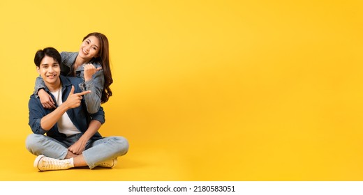 Two Young good looking asian couple isolated on yellow background sitting and relax pointing at copy space - Shutterstock ID 2180583051
