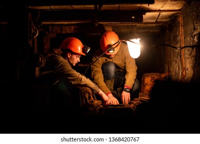 Two young guys in a working uniform and protective helmets, sitting in a low tunnel. Workers of the mine. Miners