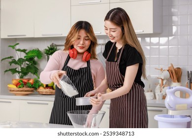 Two young happy Asian beautiful woman, female wearing aprons intends and headset standing in kitchen sifting flour for homemade bakery, bread baking making pastry. Lifestyle enjoy cooking at home - Powered by Shutterstock