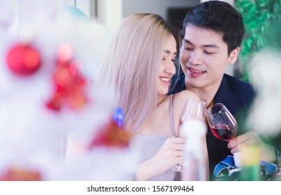 Two Young Happy Asian Couple Holding Wine Glasses In Private Home Party. Young Asian Lover Couple Drinking Wine For New Year 2020 & Christmas Celebration. They Also Celebrate Wedding Anniversary Too.