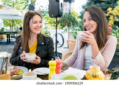 Two Young Happy Brunette Women Friends In Casual Clothes Having Fun And Laughing During Brunch In Cafe Outside On Sunny Day.