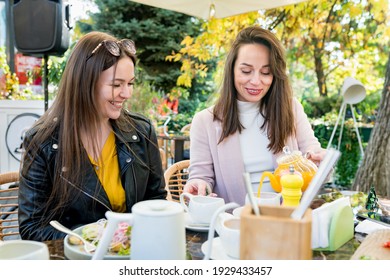 Two Young Happy Brunette Women Friends In Casual Clothes Having Fun And Laughing During Brunch In Cafe Outside On Sunny Day.