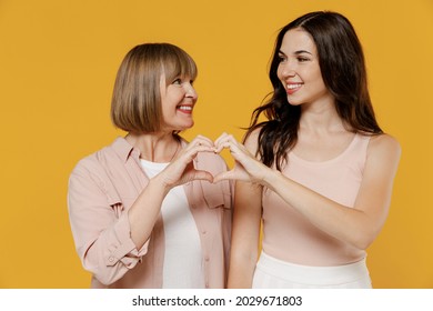 Two young happy lovely daughter mother together couple women wearing casual beige clothes showing shape heart with hands heart-shape sign isolated on plain yellow color background studio portrait.