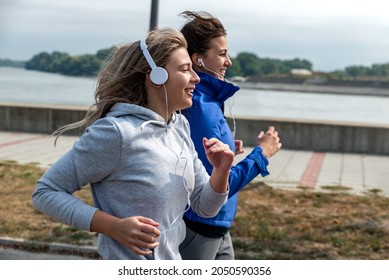 Two Young Happy And Self Loved Woman The Best Friends Jogging And Running Outdoor Near The River For Health Life Doing Bodyweight Workout And Training By Jog Together While They Listening To Music 