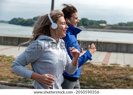 Two young happy and self loved woman the best friends jogging and running outdoor near the river for health life doing bodyweight workout and training by jog together while they listening to music 