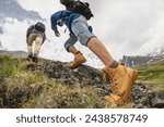 Two young hikers with backpacks walks in mountains. Close up photo of tourist legs going uphill