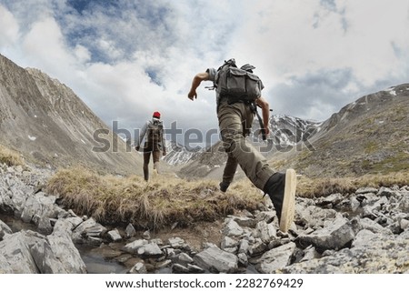 Two young hikers walks with light backpacks in mountains. Tourist jumps across the obstacle