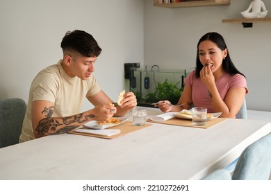 Two Young Hispanic People Eating Traditional Arepas In The Living Room.