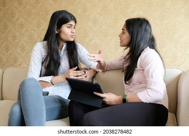Two young Indian girls having discussion while using a digital tablet at home