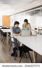 Two young Indian managers working on online business project together, using laptop for Internet communication, discussing Internet marketing strategy, cooperation, partnership