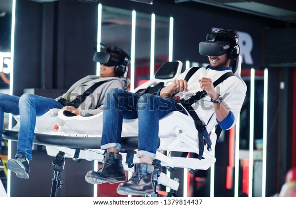 Two young indian\
people having fun with a new technology of a vr headset at virtual\
reality simulator.
