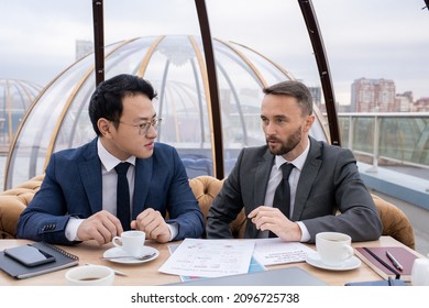 Two Young Intercultural Business Partners Having Tea And Planning Work While Having Meeting By Table In Cafe