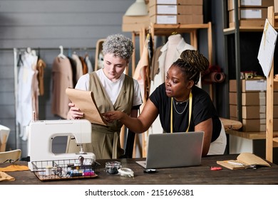 Two young intercultural seamstresses discussing new sketch of attire - Powered by Shutterstock