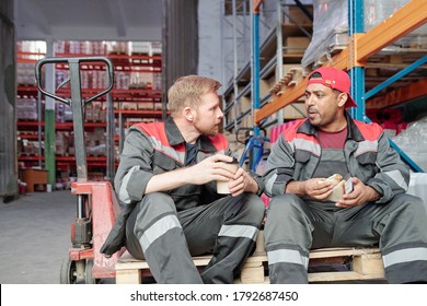 Two Young Intercultural Workers Sitting On Industrial Cart In Warehouse Environment And Discussing After Work Plans At Lunch Break