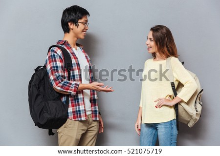Two young interracial students with backpacks talking isolated on the gray background