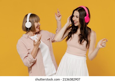 Two young joyful happy daughter mother together couple women in casual beige clothes headphones listen to music dance isolated on plain yellow color background studio portrait Family lifestyle concept