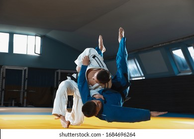 Two young judo caucasian fighters in white and blue kimono with black belts training martial arts in the gym with expression, in action, motion. Practicing fighting skills. Overcoming, reaching target