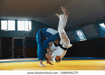 Two young judo caucasian fighters in white and blue kimono with black belts training martial arts in the gym with expression, in action, motion. Practicing fighting skills. Overcoming, reaching target