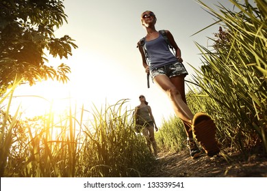 Two young ladies with backpacks walking through green tropical meadow
