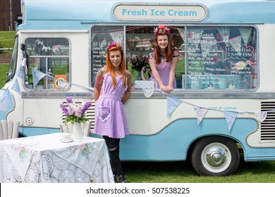Two young ladies with red hair wearing vintage spotted dresses and flower headbands standing with ice cream van next to lavender flower display