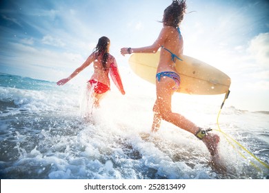 Two Young Ladies Surfers Running Into The Sea With Surf Boards