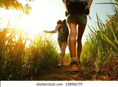 Two young ladies walking with backpacks through green lush meadow